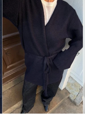 Svart omlottkofta - Snygg svart omlottkofta med knytband i midjan och lång ärm. Koftan har en enkel, rak passform och är tillverkad i ett mjukt, stickat material. Perfekt att slänga över en t-shirt eller linne för en chill look.