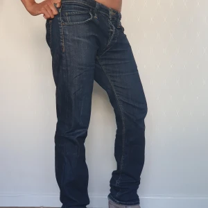 Mörkblå raka jeans med kontrastsömmar - Säljer ett par mörkblå baggy jeans med raka ben och klassiska kontrastsömmar. Jeansen har fem fickor och normal midja. Perfekta för dig som gillar en tidlös och enkel stil. Materialet är kraftigt denim som håller formen. Stängs med knappar. Har en lösare passform i storlek S.