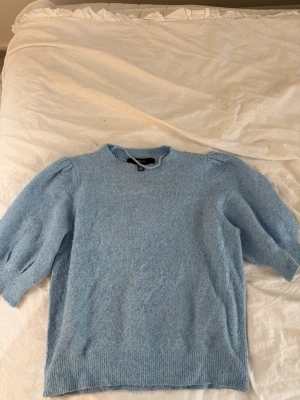 Ljusblå stickad tröja Vero Moda - Söt ljusblå stickad tröja från Vero Moda med puffärmar och ribbade muddar. Tröjan har rund halsringning och är gjord i ett mjukt, fluffigt material som känns riktigt mysigt. Perfekt för att addera lite färg till din vardagsstil.