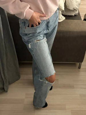 Ljusblå raka jeans med slitningar - Säljer ett par ljusblå/urtvättad blå jeans från Gina Tricot med hög midja och slitningar vid knä och lår. Jeansen har raka ben och klassiska fem fickor. Perfekta för en avslappnad och trendig look. Endast använda en gång så i nytt skick! 