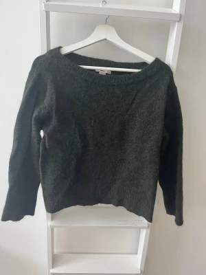 Mörkgrön stickad tröja från Gina Tricot - Mysig mörkgrön stickad tröja från Gina Tricot med bred ribbad halsringning och ribbade muddar vid ärmslut och nederkant. Tröjan har en avslappnad passform och materialet är mjukt och fluffigt, vilket gör den extra skön. Köparen står för eventuell frakt. 