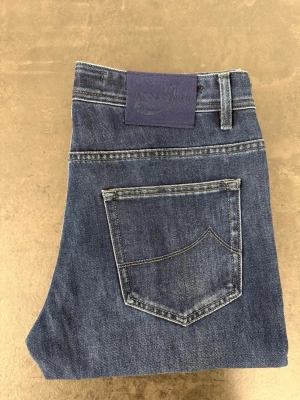 Mörkblå raka jeans från Jacob Cohen W32 - Säljer ett par klassiska mörkblå jeans från Jacob Cohen. Jeansen har rak passform, fem fickor och snygga kontrastsömmar. Tillverkade i slitstark denim med en stilren look och diskret logga på bakfickan. Perfekta för en avslappnad och trendig stil.