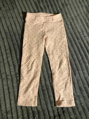 Ljusrosa leggings med guldprickar - Supersöta ljusrosa leggings med små guldstjärnor över hela tyget. De har resår i midjan och fejkfickor fram samt riktiga bakfickor. Mjukt och stretchigt material som sitter skönt. Perfekta för dig som gillar en söt och trendig look.
