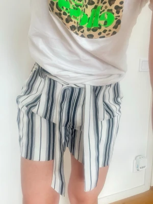 Randiga shorts med knytband - Snygga shorts med svartvita ränder och knytband i midjan. Modellen är högmidjad och har en lös passform, perfekt för varma dagar. Shortsen har fickor på sidorna och är tillverkade i ett mjukt bomullsmaterial.