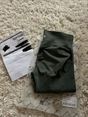 Mörkgröna seamless leggings DFYNE - Snygga gröna/beige seamless leggings från DFYNE med medel midja och scrunch-detalj bak. Impact modellen som formar kropp och rumpa snyggt! Säljes så de var för korta för mig som är 175cm. Endast testade en gång🙏🏼 Säljer även ett par likadana i annan färg och i XS!🌸