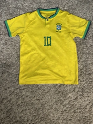 Brasilien Neymar Jr matchtröja gul - Säljer en gul Brasilien matchtröja från Nike med gröna detaljer, nummer 10 och Neymar Jr på ryggen. Tröjan har korta ärmar, rund hals och är tillverkad i lätt, ventilerande material som passar perfekt till fotbollsträning eller match.