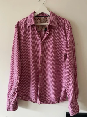 Rutig skjorta från Scotch & Soda - Säljer en röd- och vitrutig skjorta från Scotch & Soda. Skjortan har klassisk krage, långa ärmar och knäppning framtill. Insidan av kragen har ett blommigt tyg som ger en unik touch. 