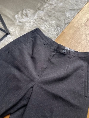 Kostymbyxor med diskreta ränder - Mörka kostymbyxor med diskreta tunna ränder. Rak passform. Ränderna är lite glansiga. 