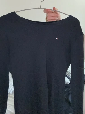 Svart långärmad topp Tommy Hilfiger - Snygg svart långärmad topp från Tommy Hilfiger med diskret logga på bröstet. Klassisk och enkel design med rund halsringning, perfekt att matcha till olika outfits. Materialet känns mjukt och stretchigt.