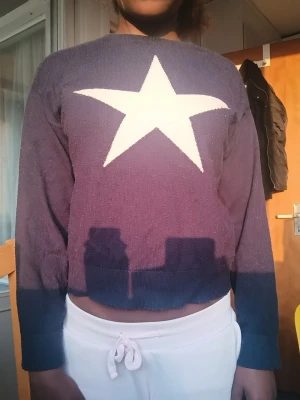 Mörkblå stickad tröja med stjärna - Cool mörkblå stickad tröja med stor vit stjärna på bröstet. Tröjan har lång ärm och en något croppad passform. Perfekt för dig som gillar statement-plagg och vill sticka ut lite extra.