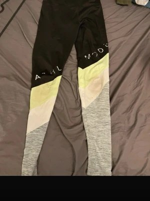 Flerfärgade leggings från HM - Snygga leggings från Hm med svart överdel, ljusgrön och vit panel samt gråmelerade ben. Stretchigt material som passar perfekt till träning eller chill. Textdetaljer på låret för extra stilpoäng.