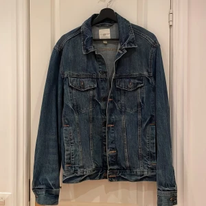 Blå jeansjacka från H&M L.O.G.G. - Klassisk blå jeansjacka från H&M L.O.G.G. i storlek S. Jackan har två bröstfickor med knappar, sidfickor och snygga kontrastsömmar. Rak passform med krage och knäppning framtill. Perfekt för dig som gillar en tidlös streetstil.