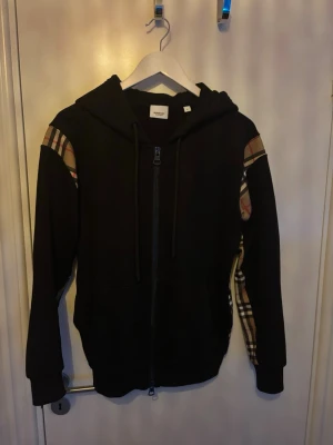 Svart hoodie med Burberry-detaljer - Säljer en svart hoodie med dragkedja från Burberry. Byten tas också emot!