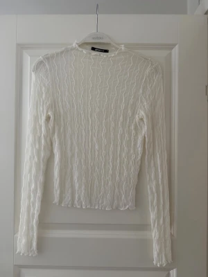 Vit genomskinlig långärmad topp från Gina Tricot - Säljer en vit långärmad topp från Gina med vågigt ribbat mönster. Toppen är lätt transparent och har en kroppsnära passform. Använd en gång!