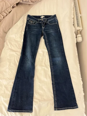 Mörkblå bootcut jeans med kontrastsömmar - Snygga mörkblå bootcut jeans med vita kontrastsömmar och låg midja. Klassisk femficksmodell med detaljerade bakfickor och slitningar framtill för en cool look. Perfekta till sneakers eller boots.