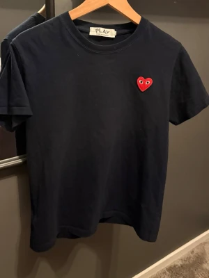 Marinblå t-shirt Comme des Garçons Play - Snygg marinblå t-shirt från Comme des Garçons Play med det ikoniska röda hjärtat broderat på bröstet. Storlek M sitter som S! Vet ej om tröjan är äkta.