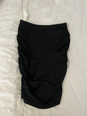 Svart draperad kortkjol - Säljer en svart & en vit kjol med snygga draperingar och rynkade detaljer längs sidorna. Kjolen har en tight passform och är perfekt för dig som vill ha en stilren men ändå trendig look. Tillverkad i mjukt syntetmaterial som sitter skönt på kroppen.