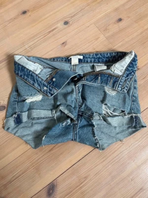 Blå  jeansshorts med slitningar - Säljer ett par blå jeansshorts med slitna detaljer Shortsen har en låg midja och dragkedja fram. Perfekta för sommaren!🩷🩷🩷