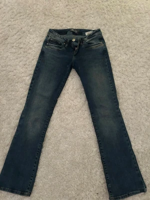 Blå bootcut jeans från LTB - Säljer ett par klassiska blå bootcut jeans från LTB med fem fickor och snygga slitningar. Jeansen har normal midja och stängs med knapp och dragkedja. Perfekta till en avslappnad stil och passar till det mesta i garderoben.