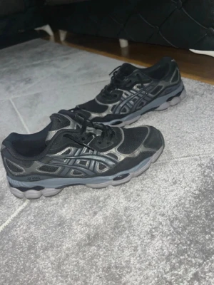 Svarta Asics Gel Nyc  - Snygga svarta Asics sneakers med grå och silverfärgade detaljer. Skorna har en sportig vibe med mesh och syntetmaterial i ovandelen samt en robust grå sula. Perfekta för dig som gillar streetstyle och bekväma skor. Skorna är i storlek 43,5 och de är bara testade. De är perfekt för sommaren.                                                                           Kontakta mig gärna ifall ni undrar något☺️