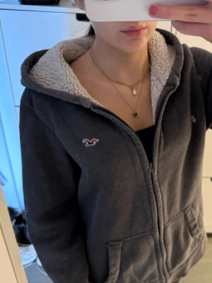Fodrad Hollister zip up hoodie - Vintage mörkgrå fodrad Hollister-hoodie med dragkedja. Storlek S! Fodrad på insidan och har Hollisters fågellogga på bröstet! Mycket bra skick, men snöret i huvan saknas och det finns ett litet fel på armen (sista bilden). Följ för fler liknande kläder och köp bundle!