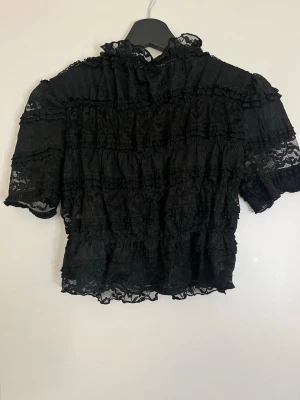 Svart spetsblus med polo krage - Jätte fin svart blus i spets med volangdetaljer och hög krage. 