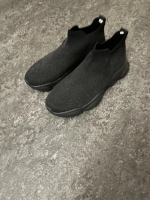 Svarta stickade sock sneakers - Svarta sneakers med stickad ovandel och chunky sula. Modellen är strumpliknande med högt skaft och minimalistisk design. Perfekta för en clean och modern streetstyle-look. Materialet är mjukt och följsamt för extra komfort.