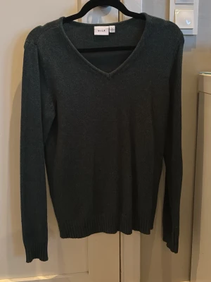 Mörkgrön stickad tröja från VILA - Mörkgrön stickad tröja från VILA med v-ringning och långa ärmar. Tröjan har ribbstickade muddar vid ärmslut och nederkant, vilket ger en snygg och enkel look. Perfekt för lager-på-lager och passar till jeans eller kjol. Hör av dig vid frågor!🥰🤍Nypris 399kr✨