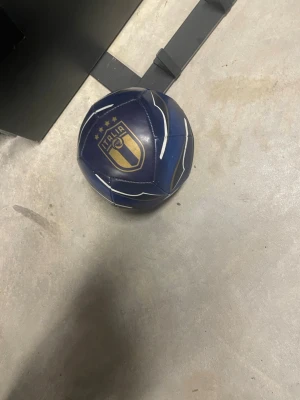 Blå fotboll för teknik med Italia-emblem - Säljer en blå fotboll med guldigt Italia-emblem och fyra stjärnor. Bollen har vita och svarta detaljer och är tillverkad i konstläder. Perfekt för dig som gillar fotboll och vill visa stöd för Italien.