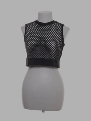 Svart croppad nätlinnetopp - Säljer en svart croppad linnetopp i nätmaterial. Toppen är ärmlös och har breda muddar vid hals och nederkant. Perfekt för att styla över ett linne eller bikini för en edgy look.