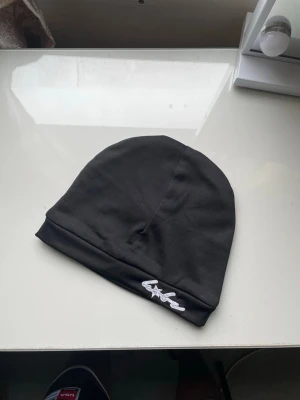 Beanie mössa - Svart mössa från Babe med vit broderad logga och stjärndetalj framtill. Tillverkad i mjukt och stretchigt material som sitter skönt på huvudet. Enkel och clean design för bara 99kr