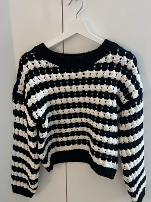 Randig stickad tröja från Lindex - Säljer en svartvit grovstickad tröja från Lindex i storlek XS. Tröjan har breda ränder, hålmönster och ribbstickad hals, ärmslut och nederkant. Perfekt för dig som gillar en avslappnad men trendig look. Tröjan är croppad.