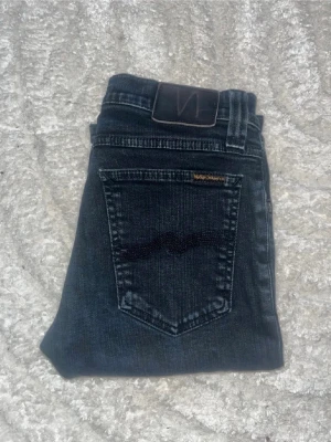 Nudie jeans - Snygga mörka jeans från Nudie Jeans, modell tight long John. Midja 34cm, längd 101cm. JAG SKICKAR EJ FLER BILDER NÄR JAG BÄR JEANSEN! för bättre inblick i passformen rekommenderar jag att googla på modellnamnet. För storleksguide kolla måtten noggrant då jeansen alltid kan vara uppsydda heller krympta och jag ej tar emot returer :) s6,4