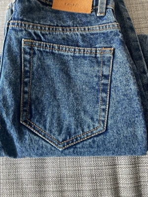 Blå raka jeans från GRUNT - Klassiska blå jeans från GRUNT i rak modell med kontrastsömmar och bakficka. Jeansen är tillverkade i slitstark denim och har en tidlös look som passar till det mesta. Perfekta för dig som gillar enkel och clean stil.