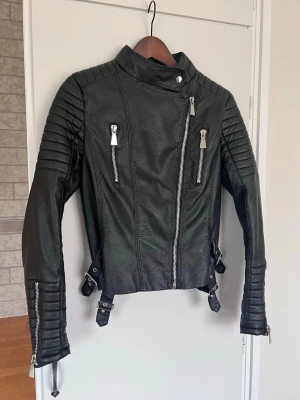 Y2K biker jacket svart faux leather – moto / 2000s / edgy - Svart bikerjacka i faux leather med silverdragkedjor och ribbade detaljer på ärmarna. Väldigt Y2K / 2000s vibe och perfekt för en edgy outfit.  Figurnära modell som passar till allt – jeans, mini skirt eller cargo pants.  Säljs då den inte kommer till användning. Notera att innertyget har gått sönder (se bäst sista bilden) men det är inget som påverkar funktionen eller syns när jackan sitter på.  📏 Storlek: 40 ✨ Skick: Mycket bra skick (fler bilder finns!!!)