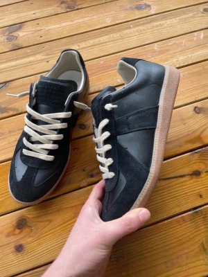 Svarta sneakers med beige sula - Stilrena svarta sneakers med beige gummisula och vita snören. Ovandelen är i en mix av mocka och slätt läder, vilket ger en snygg kontrast. Klassisk låg modell som passar till många olika stilar.