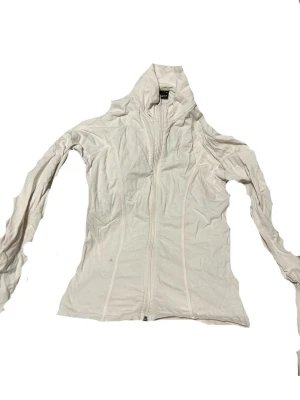 Vit ziphoodie med hög krage - Vit ziphoodie med hög krage. Modellen är figursydd. Tillverkad i mjukt bomullsmaterial som känns skönt mot huden. Perfekt för en avslappnad och enkel stil. Passar M-L