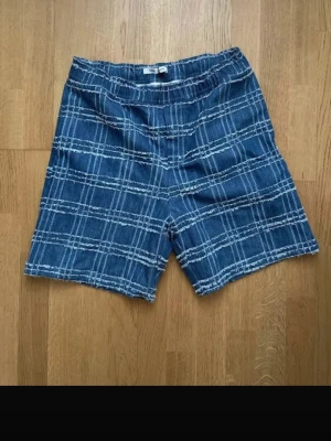 Blå rutiga shorts från Samsøe Samsøe - Säljer ett par blå shorts från Samsøe Samsøe med vitt rutmönster. Shortsen har en avslappnad passform och elastisk midja för extra komfort. Perfekta för varma dagar och en cool, avslappnad stil. Nypris 1200