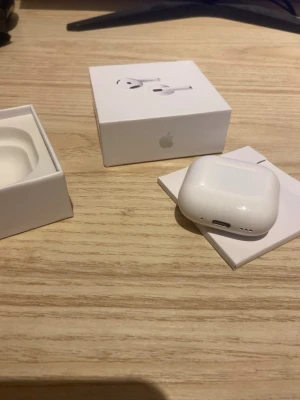 Airpods 4 - Säljer ett par Apple AirPods 4 i klassisk vit färg med tillhörande laddningsetui. Trådlösa in-ear-hörlurar med stilren och kompakt design, perfekt för musik och samtal. Levereras i originalförpackning med allt som syns på bilden.