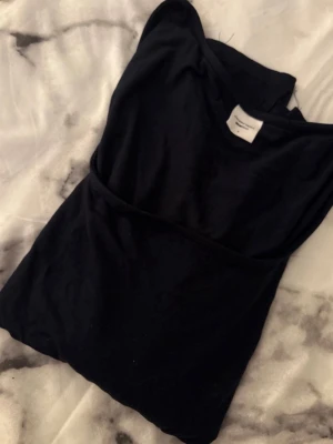 Svart topp från Gina Tricot - En svart enkel topp från Gina Tricot, kollektionen Elevated Basics. Topp i klassisk modell med rund halsringning, tillverkad i mjukt bomullsmaterial. Perfekt att styla med jeans eller kjol.