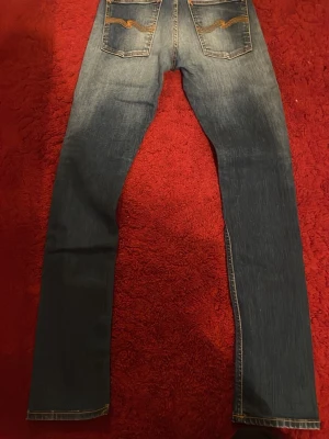 Nudie - Säljer ett par klassiska blå jeans med slim fit och snygg tvätt framtill. Jeansen har fem fickor och kontrastsömmar. Perfekta för en avslappnad och trendig look. Pris kan diskuteras! 