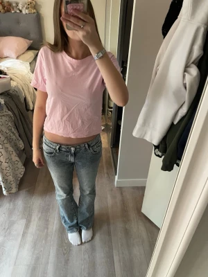 Ljusrosa t-shirt från Lindex - En enkel och stilren ljusrosa t-shirt från Lindex. T-shirten har rund halsringning och korta ärmar. Tillverkad i mjuk bomull som känns skön mot huden. Perfekt att matcha med jeans eller kjol för en avslappnad look.