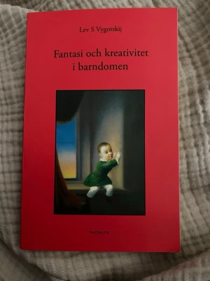 Fantasi och kreativitet i barndomen - En bok av Lev S Vygotskij med röd mjukpärm och omslagsbild av ett barn vid ett fönster. Boken utforskar fantasi och kreativitet hos barn och är en klassiker inom psykologi och pedagogik. Perfekt för dig som är intresserad av barns utveckling och lärande.