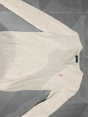 Ljus beige tröja från Polo Ralph Lauren - Tröjan är i st M men är ganska liten i storleken. Ljus beige stickad tröja från Polo Ralph Lauren med V-ringning och lång ärm. Tröjan har en liten rosa broderad logga på bröstet och ribbade muddar vid ärmslut och nederkant. Perfekt för dig som gillar klassisk och stilren design.