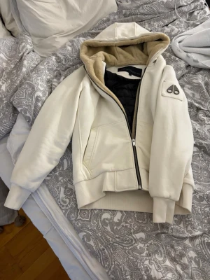 Vit pufferjacka från Moose Knuckles - Snygg vit pufferjacka från Moose Knuckles med beige päls i huvan och svart quiltat innerfoder. Jackan har dragkedja, två fickor fram och logotyp på ärmen. Perfekt för kalla vinterdagar och riktigt trendig look. Köpt på Room 1006 på emporia i Malmö för 4 599kr kvitto med påse finns! Pris kan diskuteras vid snabb affär!