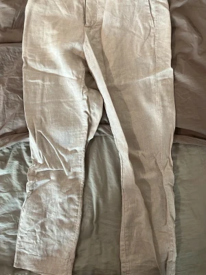 Beige linnebyxor med raka ben - Snygga beige linnebyxor med raka ben och klassisk passform. Byxorna har bälteshällor och två bakfickor med minimalistisk design. Perfekta för en avslappnad men ändå stilren look. Tillverkade i svalt linnematerial.