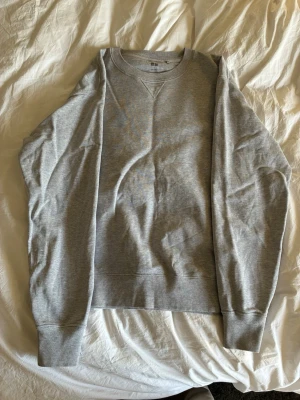 Grå sweatshirt från Uniqlo - Klassisk grå sweatshirt från Uniqlo med rund halsringning och ribbade muddar vid ärmslut och nederkant. Tröjan har en enkel och stilren design. Perfekt för en avslappnad och snygg look.