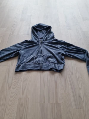 Grå velour hoodie med dragkedja från Hollister - Mjuk och skön hoodie i grå velour med dragkedja framtill och två fickor. Modellen är croppad och har en stor huva. Perfekt för en avslappnad och trendig look.