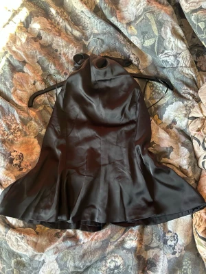 Svart halterneck topp i satin - Snygg svart halterneck topp från Gina Tricot i glansigt satinmaterial. Toppen har en utsvängd nederdel och knytning i nacken för en chic siluett. Perfekt för dig som vill ha en trendig och elegant look.