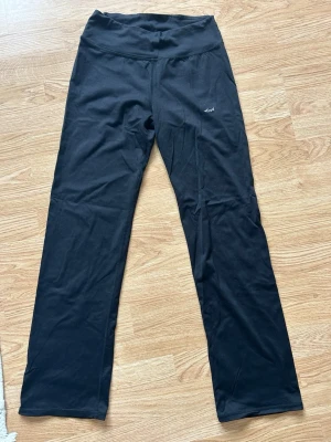 Svarta vida leggings från Röhnisch - Snygga svarta leggings från Röhnisch med hög midja och raka ben. Tillverkade i ett stretchigt och mjukt material som passar perfekt till träning eller chill. Diskret logga på låret. Klassisk och enkel design som är lätt att matcha.
